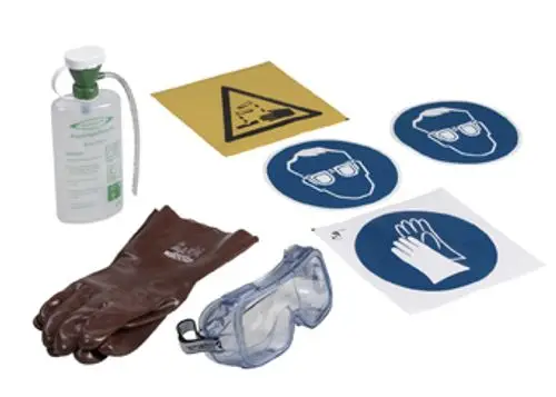 Sicherheitspaket mit Schutzhandschuhen, Schutzbrille, Sicherheitszeichen und einem Behälter, erkennbar mit Produkten der Marke Grünbeck für den Umgang mit ätzenden Stoffen.